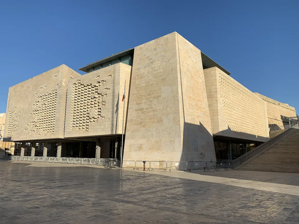 Здание парламента Мальты в Валлетте из светлого камня, перед ним площадь и флаг
