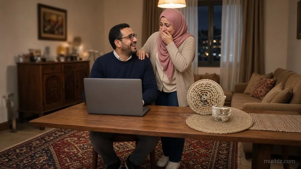 يجلس كريم بنظارته وكنزته الكحلية إلى طاولة الطعام أمام حاسوب محمول، وتقف أمل بحجابها الوردي خلفه، يدها على كتفه ويدها الأخرى على فمها من الفرحة